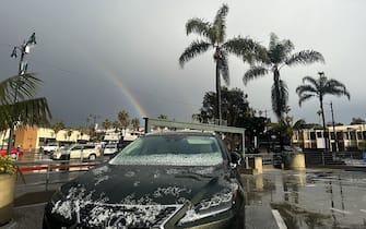 A rainbow appears between palm trees as hail partially covers a vehicle during a winter storm that blanketed the region with rain, snow, and hail in Redondo Beach, California, on February 25, 2023. - Heavy snow fell in southern California as the first blizzard in a generation pounded the hills around Los Angeles, with heavy rains threatening flooding in other places. (Photo by Patrick T. Fallon / AFP) (Photo by PATRICK T. FALLON/AFP via Getty Images)