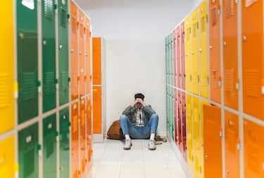 Sad pensive teenager sitting alone in the floor in locker room.