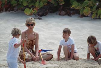 Diana, Princess of Wales (1961 - 1997) holidaying with her sons Prince William and Prince Harry and her sister's children on Necker Island in the British Virgin Islands, 11th April 1990. The island is owned by Virgin chairman Richard Branson. Diana is wearing a leopard print swimsuit while Prince William (second from right) buries her in sand. (Photo by Tim Graham Photo Library via Getty Images)
