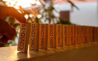 Hand poked on a row of wooden dominoes, with the words "COVID19" on the first piece and the words "LONG COVID" on subsequent pieces.