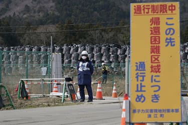 A sign for a "difficult-to-return" designated zone is displayed next to a security officer standing guard in front of bags of contaminated soil in Namie, Fukushima Prefecture, Japan, on Monday, March 8, 2021. Laid waste by a nuclear disaster a decade ago, Japans Fukushima is still struggling to recover, even as the government tries to bring people and jobs back to former ghost towns by pouring in billions of dollars to decontaminate and rebuild. Photographer: Toru Hanai/Bloomberg via Getty Images