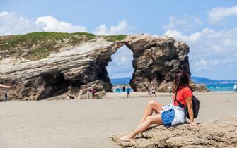 Ribadeo, Lugo, Spain, Europe. June 20, 2023 A tourist at the famous beach of the cathedrals. The rocks that compose it are mainly slate and quartzite. The rough waters of the Cantabrian Sea, has sculpted amazing shapes in the cliffs, creating long passages carpeted with fine sand, deep caves with beautiful colors, which are changing depending on the orientation of the sun, large arches over 30m high. The beach of the Cathedrals is of fine sand, it has a length of 1400m...