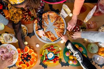 A buffet on a dining table at halloween in North East England. Unrecognisable people are wearing fancy dress and reaching for snacks on the table.