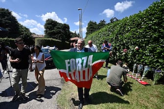 A mourner holds a Forza Italia party flag near flowers layed in tribute outside Villa San Martino, the residence of Italian businessman and former prime minister Silvio Berlusconi, following his death, in Arcore, northern Italy, on June 12, 2023. Italy's former prime minister Silvio Berlusconi has died aged 86, his spokesman confirmed to AFP on June 12, 2023. The billionaire media mogul was admitted to a Milan hospital on June 9 for what aides said were pre-planned tests related to his leukemia. (Photo by Piero CRUCIATTI / AFP)