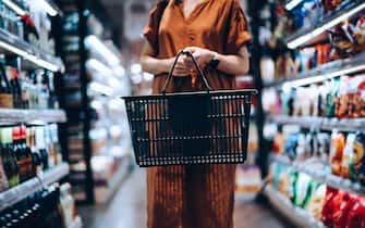 Cropped shot of young woman carrying a shopping basket, standing along the product aisle, grocery shopping for daily necessities in supermarket