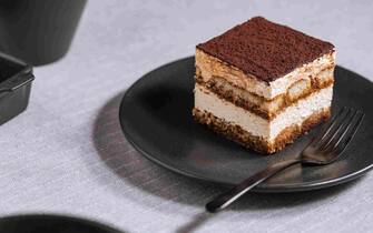 Tiramisu cake dessert on a grey background. One piece of traditional Italian dessert made from mascarpone cheese, coffee and biscuits