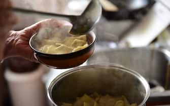 Serving tortellini into a bowl from a cooking pot using a ladle. One of the final steps in the preparation of homemade tortellini, pasta parcels stuffed with beef, egg, parmesan cheese, in a kitchen in Italy