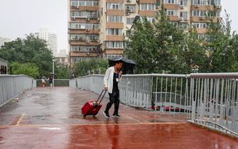 epa10776425 A man uses an umbrella during a downpour in Beijing, China, 30 July 2023. China's National Meteorological Center issued a red alert, the highest alert in multiple provinces including Beijing, as the country is expected to continue experiencing heavy rainfall brought by Typhoon Doksuri.  EPA/MARK R. CRISTINO