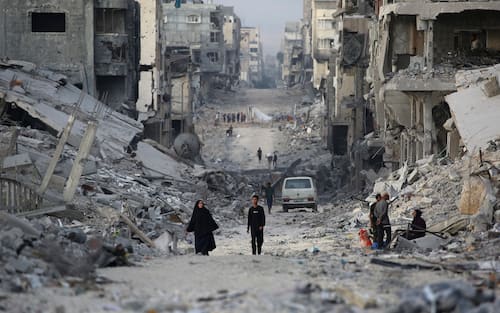 Palestinians make their way past destroyed buildings in Gaza City on October 12, 2025. Hundreds of thousands of Palestinians returned to a devastated Gaza City, after an Israel-Hamas ceasefire came into effect, and as both sides discuss implementing US President Donald Trump's 20-point plan to end the war, which calls for Hamas' disarmament and for the group not to be involved in running post-war Gaza. (Photo by Bashar TALEB / AFP)