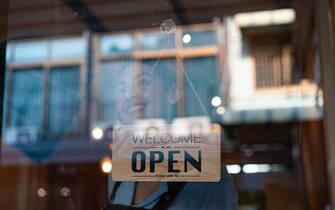 Happy business owner hanging an open sign at a cafe