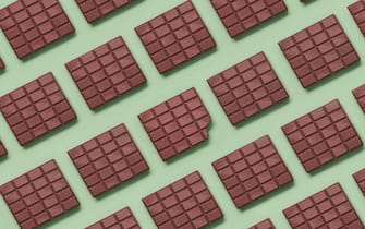 Geometric pattern made with chocolate bars and in the center a bitten tablet on green background