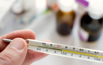 Doctor's hand holding thermometer indicating a high temperature