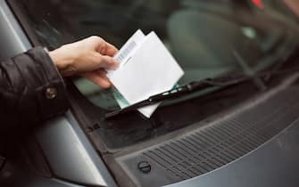 Human hand spotting parking ticket under windscreen wiper.