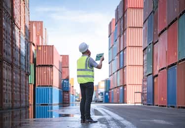 Confident Engineer and tablet at Containers yard from Cargo freight ship for import export. Dock control worker wearing protective coveralls against stack of a containers terminal. Logistic and Transportation, Global Business concepts.