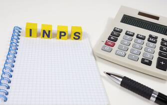 Single word "INPS" on wooden block, taxes isolated, with an office desk background.
