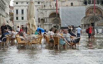 Turisti consumano bibite seduti tra i tavolini nell’acqua che ha allagato piazza San Marco, Venezia 5 settembre 2024. ANSA/ANDREA MEROLA