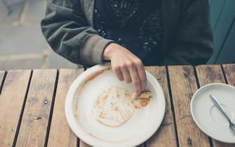 A young woman is wiping sauce off her plate with a piece of bread