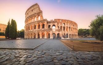 Iconic Flavian Amphitheatre, the ancient Roman Colosseum, a famous tourist landmark, illuminated at sunrise or sunset in historic Rome, Italy.