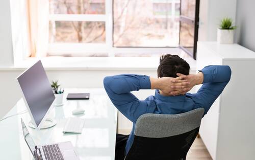Relaxed Young Businessman Relaxing On Chair Behind Desk At Office