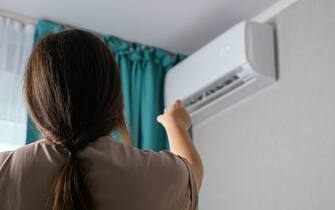 Unrecognizable woman turns on the air conditioner, back view.