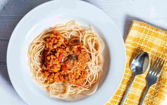 A bowl of ragu bolognaise served on a bed of spaghetti. A serving is placed on a table in a deep white bowl