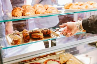 woman hand using food pliers to serve a croissants to a customer in a cafe.  Italian breakfast