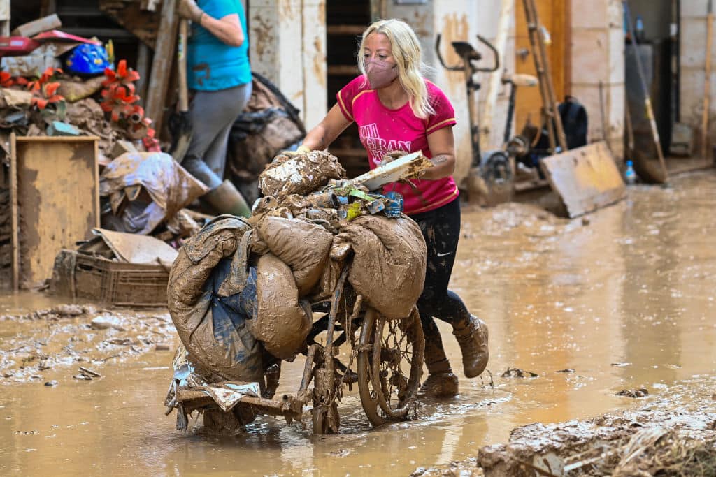 A woman pushes a wheelchair full of debris through the mud on November 2, 2024, in the aftermath of devastating floolding in the town of Paiporta, in the region of Valencia, eastern Spain. Spain will deploy 10,000 more troops and police officers to the eastern Valencia region devastated by floods that have killed 211 people, Prime Minister Pedro Sanchez said. (Photo by JOSE JORDAN / AFP) (Photo by JOSE JORDAN/AFP via Getty Images)