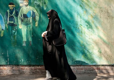 veiled muslim woman walking by revolutionary fighters mural in downtown tehran city street iran outside old US american embassy