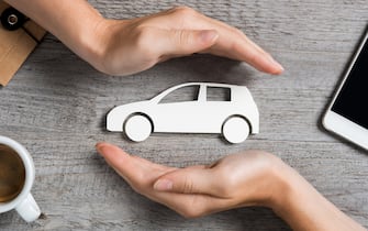 Hands protecting icon of car over wooden table. Top view of hands showing gesture of protecting car. Car insurance and automotive business concept.