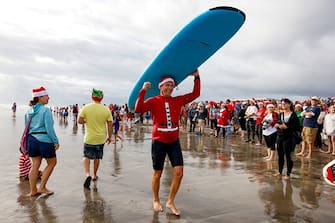 A surfer dressed as Santa carries his board during the 15th annual "Surfing Santas" event in Cocoa Beach, Florida, on December 24, 2023. (Photo by Eva Marie UZCATEGUI / AFP) (Photo by EVA MARIE UZCATEGUI/AFP via Getty Images)