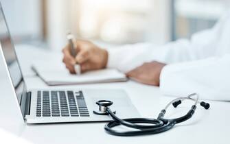 Laptop, stethoscope and doctor writing in notebook for research planning or medical tech innovation in hospital office. Healthcare medic worker, research strategy book notes and online communication