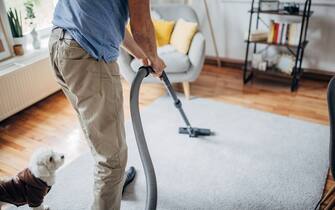 One man, old man vacuuming the carpet at home.