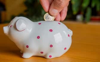 Close up of a male hand dropping a 1 Euro coin into a piggy bank