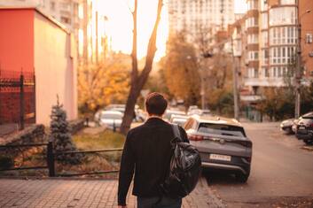 Rear view of young man with backpack walking on the city street at sunset