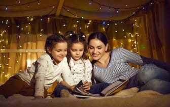 Mother with daughters children reading book spending time in home tent