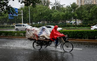 epa10776423 People ride a rickshaw during a downpour in Beijing, China, 30 July 2023. China's National Meteorological Center issued a red alert, the highest alert in multiple provinces including Beijing, as the country is expected to continue experiencing heavy rainfall brought by Typhoon Doksuri.  EPA/MARK R. CRISTINO