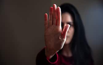 Young woman with raised hand for dissuade. Stop violence against women, sexual abuse, trafficking. Dark room background, copy space.