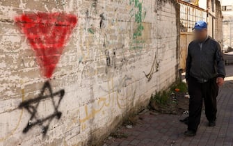 A Palestinian man walks past a graffiti of the Star of David under an inverted “red triangle”, a symbol that the Palestinian Hamas movement's military wing Al-Qassam Brigades uses to identify Israeli targets in their videos, in the occupied West Bank city of Hebron on November 30, 2023, on the seventh day of a truce between Israel and Hamas. The warring parties have agreed a pause in fighting to allow time for the militant group to release Israeli hostages in exchange for Palestinian prisoners. (Photo by HAZEM BADER / AFP)