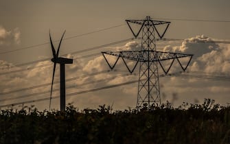 BATH, UNITED KINGDOM - JULY 16: A wind turbine generates electricity besides electrical pylons carrying electricity cables across fields on July 16, 2023 near Bath, England. The UK government has published documents with plans for Britain should it have to go â  lights outâ   this winter after the National Grid warned there could be blackouts due to the ongoing energy crisis. There are fears that Russian President Vladimir Putin will restrict gas supplies to Europe and although the UK does not rely on Russian energy supply, it does import from electricity and gas from European countries that do. With many consumers already facing a cost of living crisis with sharp rises in their home energy bills, energy blackouts look set to compound their misery this winter. (Photo by Matt Cardy/Getty Images)