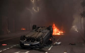 epa10717565 A fire burns next to an overturned car during clashes with French riot police following a march in the memory of 17-year-old Nahel, who was killed by French Police in Nanterre, near Paris, France, 29 June 2023. Violence broke out after the police fatally shot a 17-year-old during a traffic stop in Nanterre on 27 June. According to the French interior minister, 31 people were arrested with 2,000 officers being deployed to prevent further violence.  EPA/YOAN VALAT