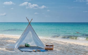 romantic white picnic tent on white sand beach with crystal clear water and blue sky at background