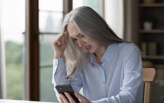 Angry nervous older businesswoman looking at smartphone screen