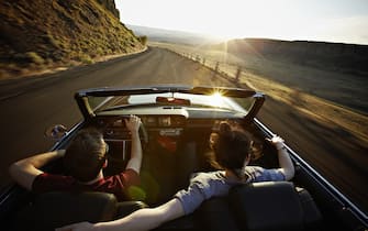 Young couple driving convertible at sunset on desert road