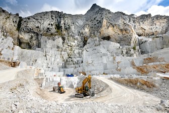 Landscape view of an open cast marble quarry in Carrara, Tuscany, Italy showing the heavy duty equipment and rock face