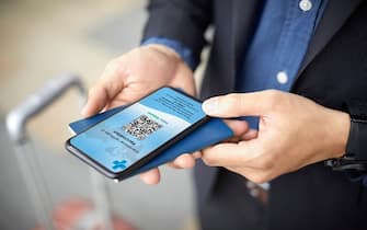 Midsection of businessman having online Covid-19 Immunization Certificate with passport. Male executive is using smart phone at airport. Traveling information is displayed on device screen.