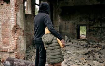 Rear view of father embracing child and looking at ruins of house after hostilities