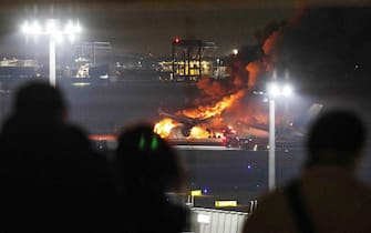 This photo provided by Jiji Press shows people on an observation deck looking at a Japan Airlines plane on fire on a runway of Tokyo's Haneda Airport on January 2, 2024. A Japan Airlines plane burst into flames on the runway of Tokyo's Haneda Airport on January 2 after apparently colliding with a coast guard aircraft, media reports said. (Photo by JIJI PRESS / AFP) / Japan OUT (Photo by STR/JIJI PRESS/AFP via Getty Images)
