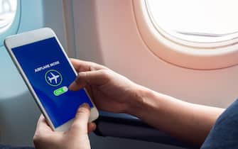 Flight mode concept. Hand holding white smartphone and turned on airplane mode on screen near the window on the airplane.