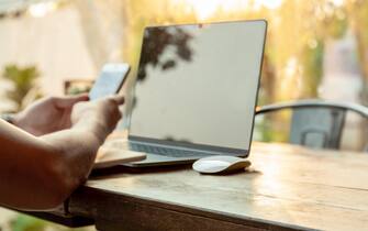 Selected focus computer mouse with man using cell phone and laptop on the table.