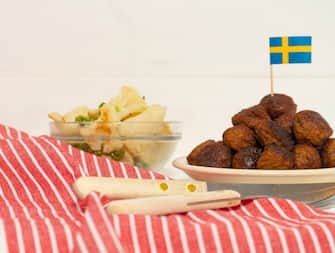 Traditional swedish meatballs (kottbullar) with cauliflower and green peas in the white plate. Swedish flags. Swedish national food concept. Background photo with place for text. Side view.
